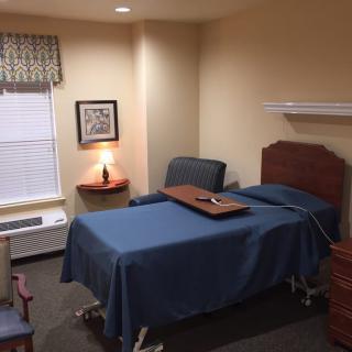 A neatly organized room featuring a hospital bed, chairs, and a lamp by the window.
