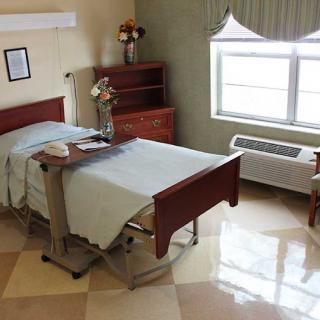 A clean and well-organized hospital room with a single bed and natural light coming through the window.