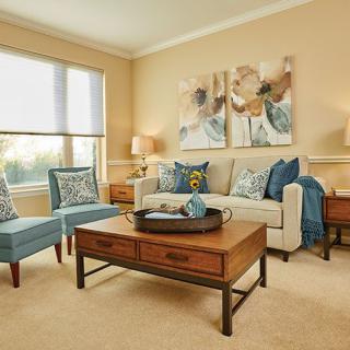 A cozy living room featuring a beige sofa with blue throw pillows, two matching armchairs, a wooden coffee table, and decorative artwork on the walls.