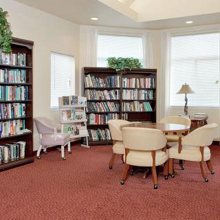 A cozy reading area in a library, featuring bookshelves, chairs, and a small table.