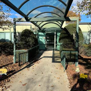 A serene walkway with a green canopy, surrounded by landscaped bushes.