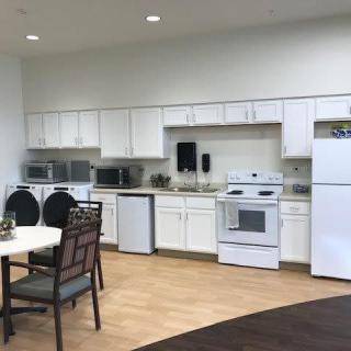 A modern kitchen with white cabinets and a dining area, featuring appliances such as a stove, refrigerator, and microwave.