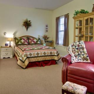 A cozy bedroom with a quilt-covered bed and a red armchair.