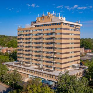 A high-rise residential apartment building surrounded by trees under a clear blue sky.