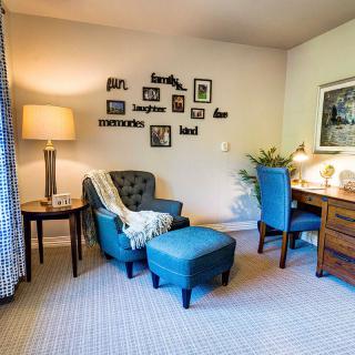 A cozy living room corner with an armchair and ottoman, a desk, and decorative wall pictures.