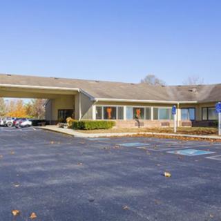 A one-story motel building with a parking lot in front, captured on a clear day.
