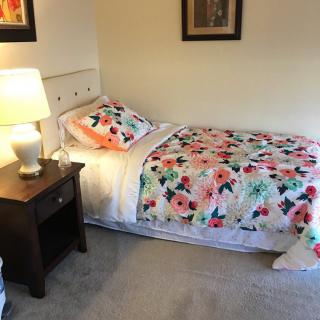 A cozy bedroom with a single bed decorated with floral bedding, accompanied by a lamp and nightstand.