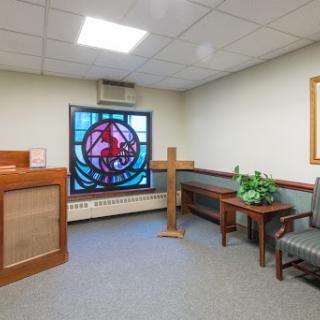 A serene interior space featuring a stained glass window and simple furnishings.