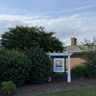 A garden sign nestled among lush greenery under a partly cloudy sky.