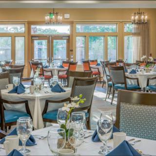 A well-decorated restaurant dining area with neatly arranged tables and chairs, featuring elegant place settings and large windows.