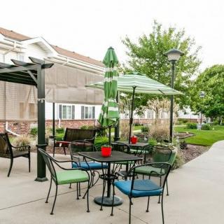 A well-maintained outdoor patio with tables, chairs, and umbrellas in a garden setting.