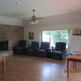 A spacious living room with a row of armchairs, a fireplace, and a large window allowing natural light to brighten the wooden-floored space.