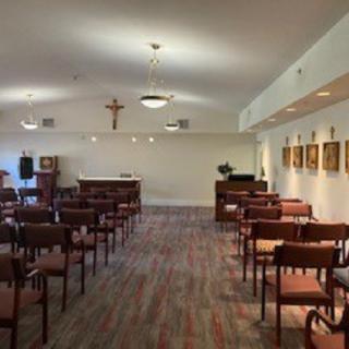 A small chapel interior with rows of chairs, religious icons, and a cross on the wall.
