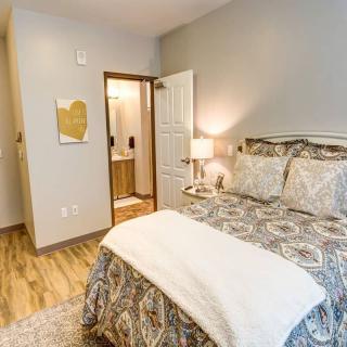A cozy bedroom with elegant bedding, a bedside lamp, and wooden flooring.
