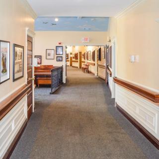 A long hallway with carpet flooring, lined with paintings and decorated walls.