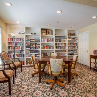 A cozy library room with bookshelves, a table, and chairs on a patterned carpet.