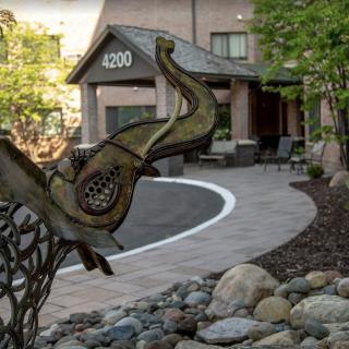 An artistic sculpture placed near the entrance of a building with landscaped surroundings.