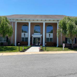 A charming building featuring classical architecture with prominent columns and large windows, surrounded by well-maintained landscaping.