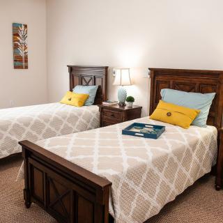 A cozy bedroom with two twin beds, featuring wooden headboards and decorative pillows, softly lit by a bedside lamp.