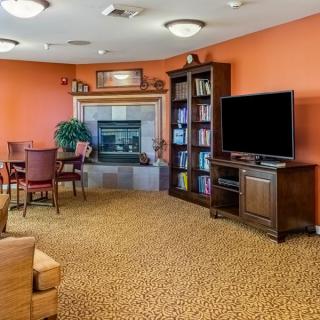 A cozy living room with orange walls, featuring a television, bookshelf, and comfortable seating.