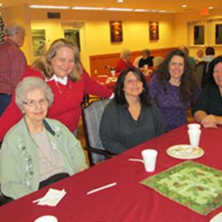 A group of people gathered around a table indoors, smiling for the camera.