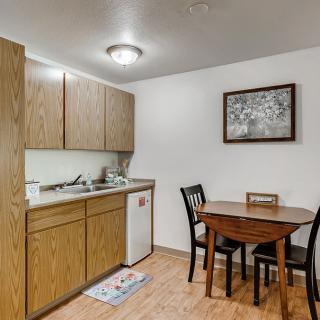 Cozy kitchen and dining area featuring wooden cabinets, a small dining table with chairs, and a decorative wall painting.