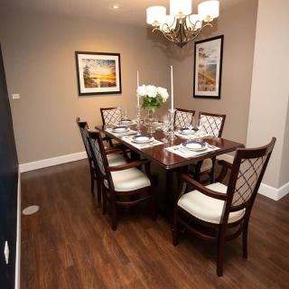 An elegantly set dining room with a wooden table, upholstered chairs, and tasteful wall art.