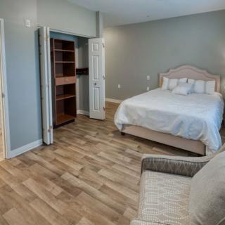 A minimalist bedroom with a neatly made bed, open closet, and wooden flooring.