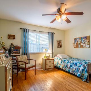 A cozy bedroom with a single bed and wooden floors, illuminated by natural light from a large window.