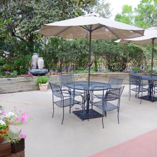 A serene patio with tables and chairs under umbrellas surrounded by lush greenery and flowers.