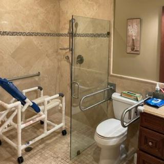 An accessible bathroom with a glass shower door, toilet, and supportive handrails.