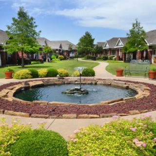 A picturesque garden courtyard with a central fountain surrounded by lush greenery and buildings.