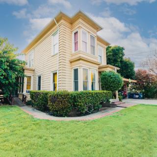 A charming two-story yellow house surrounded by a well-maintained garden and lush green lawn under a partly cloudy sky.