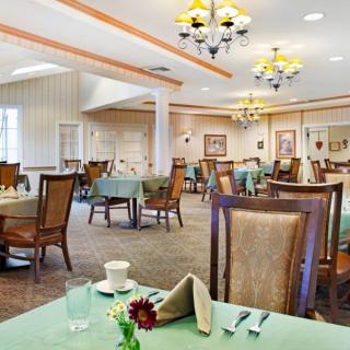 An elegant dining room with neatly arranged tables and chairs, well-lit by chandeliers.