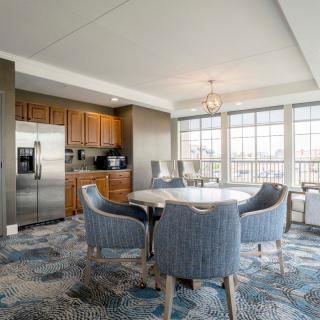 A modern dining area with a round table, comfortable chairs, large windows, and an adjacent kitchen.