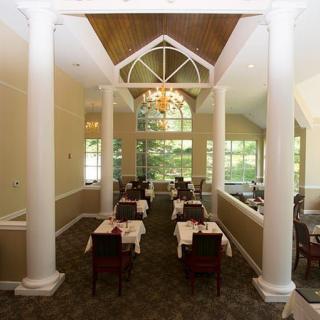 Elegant dining room with columns and a chandelier, featuring tables set for guests.