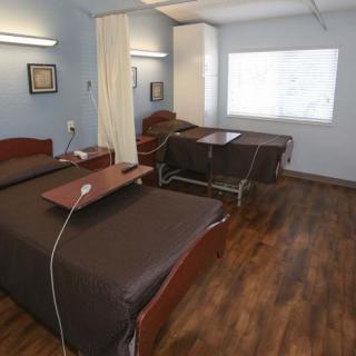 A hospital room with two patient beds, separated by a curtain, featuring wooden flooring and medical equipment.