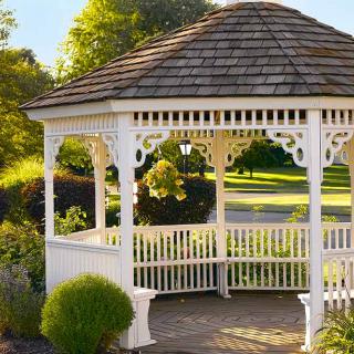A beautiful white wooden gazebo surrounded by lush greenery in a sunlit garden setting.