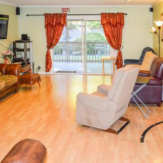 A spacious living room with comfortable seating and a television, featuring laminate flooring and large windows with red curtains.