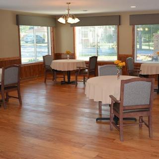 An empty dining room with several tables and chairs, featuring wooden floors and large windows.
