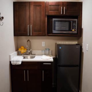 A compact kitchen setup with wooden cabinets, a microwave, refrigerator, and sink.
