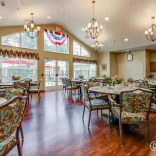 A spacious dining area with elegant chandeliers and large windows, featuring multiple tables and chairs.