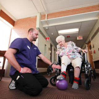 A healthcare professional assists an elderly person in a physical therapy exercise aimed at improving mobility and strength.