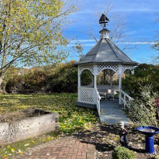 A charming gazebo situated in a serene garden, surrounded by lush greenery and a clear blue sky.