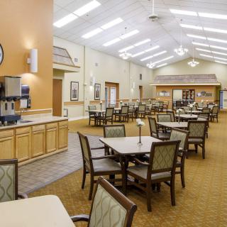 A spacious dining hall with neatly arranged tables and chairs, featuring bright overhead lighting.