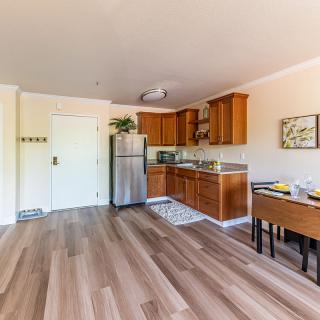A cozy apartment kitchen with wooden cabinets and flooring, featuring a refrigerator and dining area.