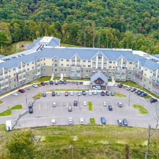 Aerial view of a hotel surrounded by lush forest with a parking lot in front.