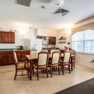 A spacious kitchen and dining area featuring a large wooden dining table with upholstered chairs, surrounded by cabinets and a window letting in natural light.