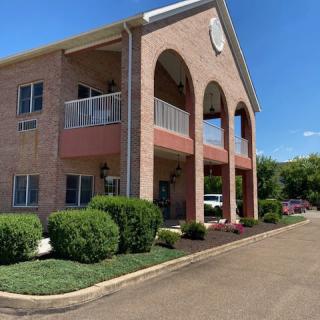 Two-story brick building with archways and balconies surrounded by well-maintained landscaping.