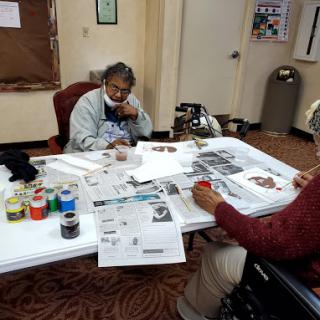Two individuals engaged in a creative art activity, working on projects at a table filled with various materials.